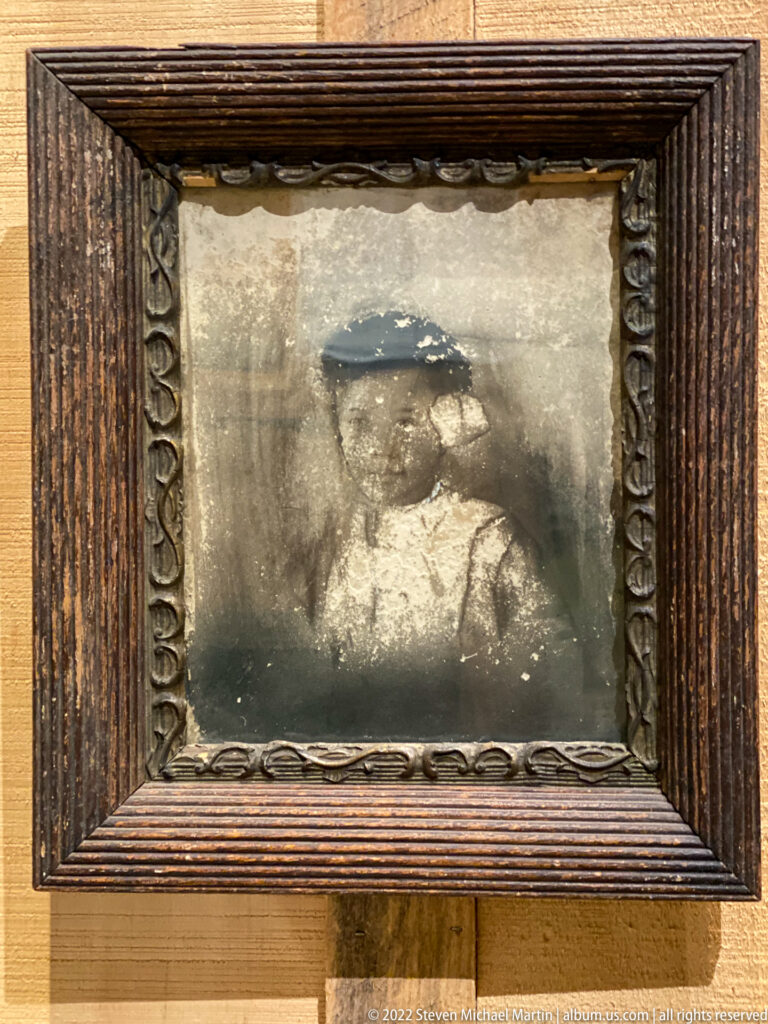 A faded portrait of a seated person appears within a deeply carved dark wood frame.
