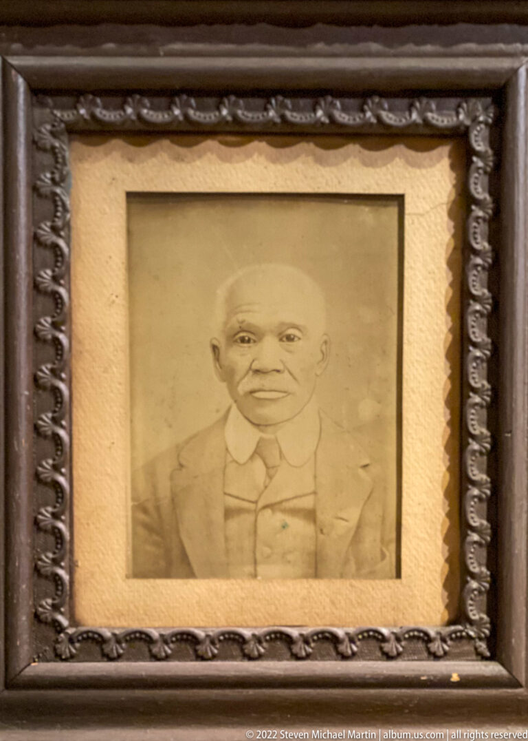 A sepia portrait shows a man in a suit and tie inside a broad mat and carved frame.