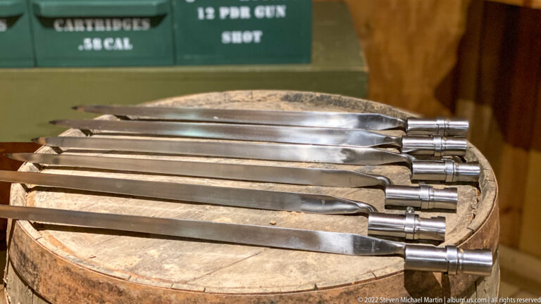 Long flat metal implements with cylindrical handles lie in parallel across a round wooden tub.