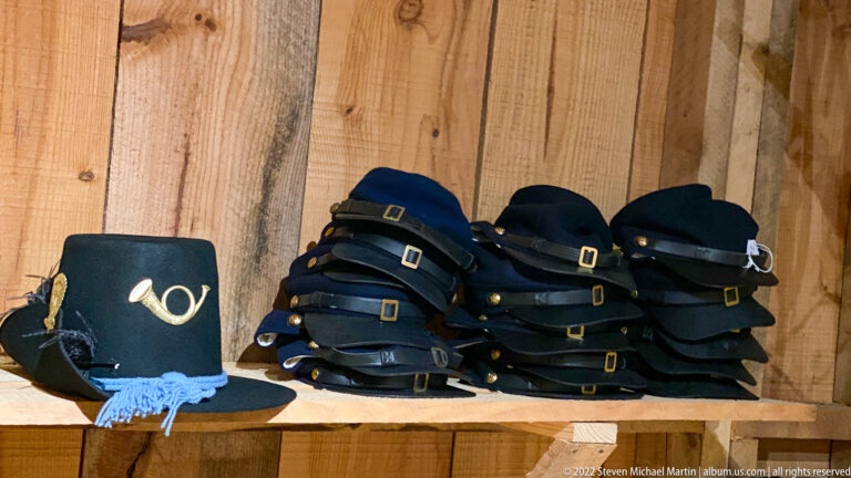 Dark military-style caps are stacked on a shelf beside a blue hat with a light-colored insignia.