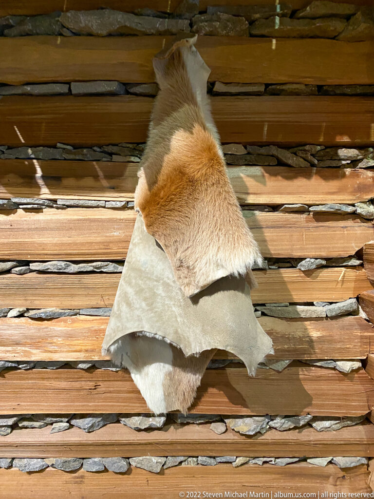 Two animal hides, one tawny and one pale, are displayed across horizontal wooden slats.