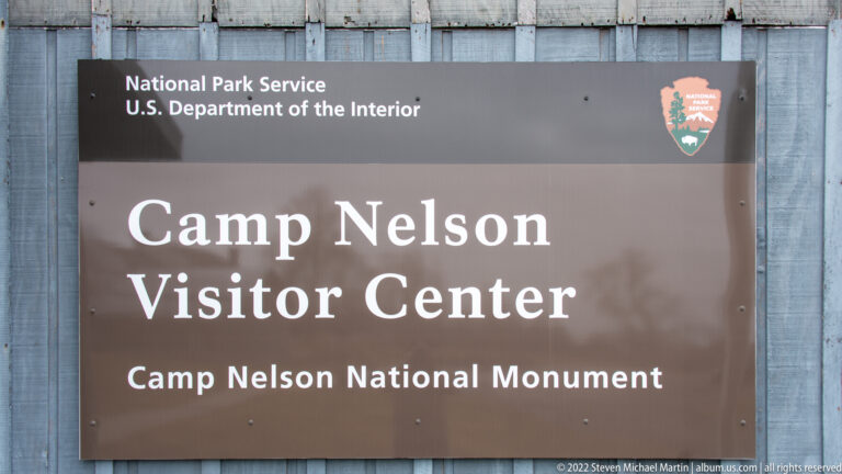 A brown sign on gray siding names the Camp Nelson Visitor Center and Camp Nelson National Monument.