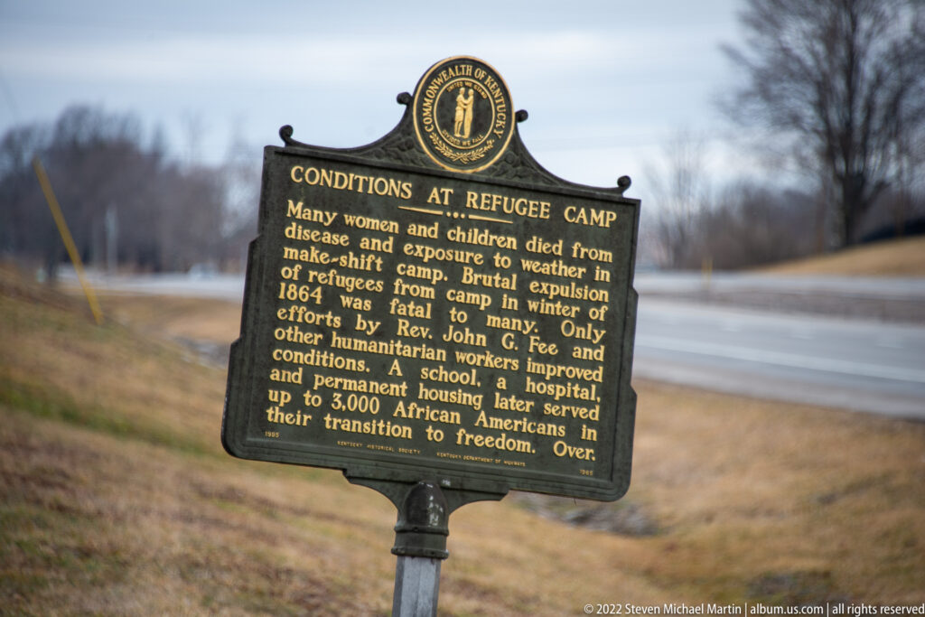 A historical marker about conditions at the refugee camp stands beside a road in a winter landscape.