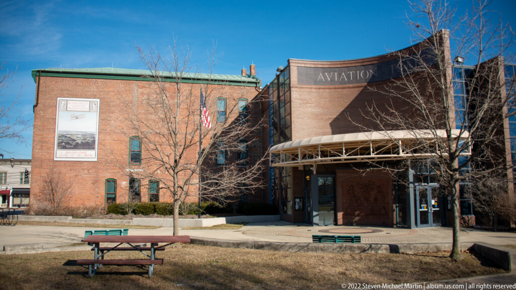 A curved brick façade marked Aviation Trail rises above a glass entrance and semicircular canopy.