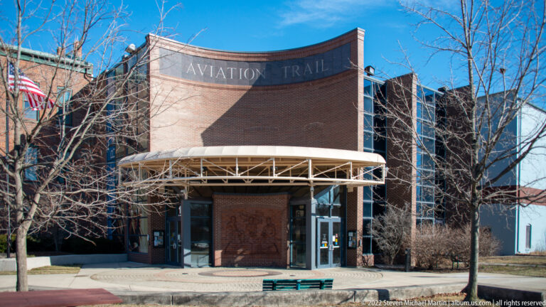 A curved brick visitor-center entrance bears the Aviation Trail name above glass doors and a white canopy.