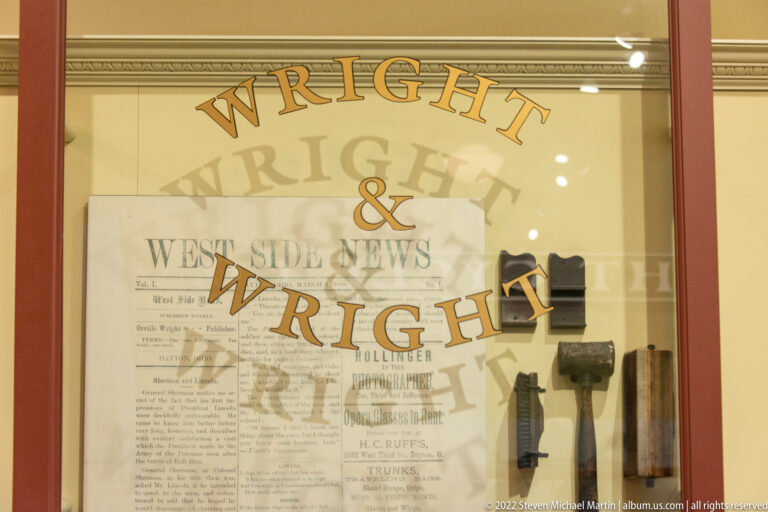 Gold “Wright & Wright” lettering overlays an old newspaper page beside printing tools in a glass case.