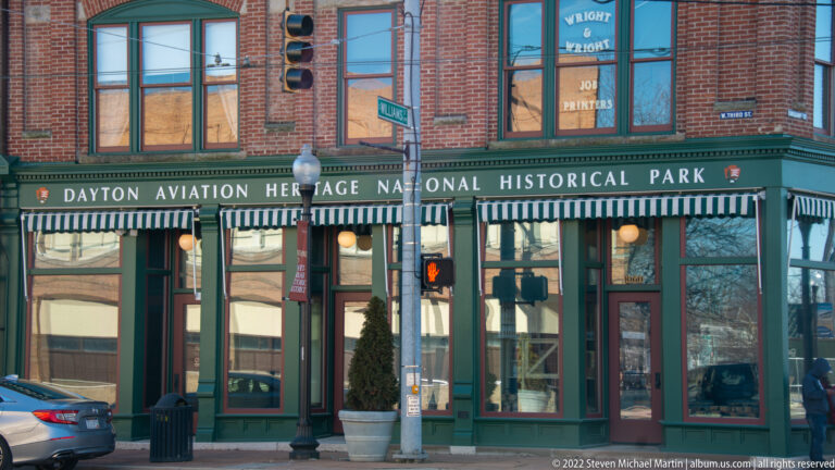 A green band on a brick storefront reads “Dayton Aviation Heritage National Historical Park” above striped awnings.