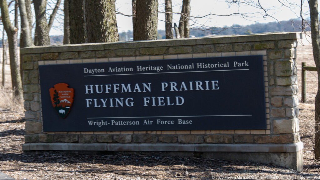 A dark sign in a stone wall names Huffman Prairie Flying Field and Dayton Aviation Heritage National Historical Park.