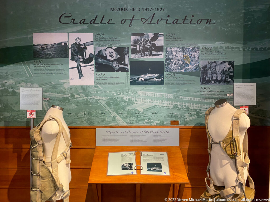 Two mannequins in flight gear stand before a McCook Field timeline with aviation photographs and a display table.
