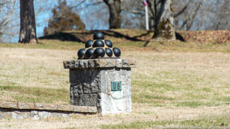 A pyramid of dark cannonballs sits atop a stone pedestal marked with a small U.S. plaque.