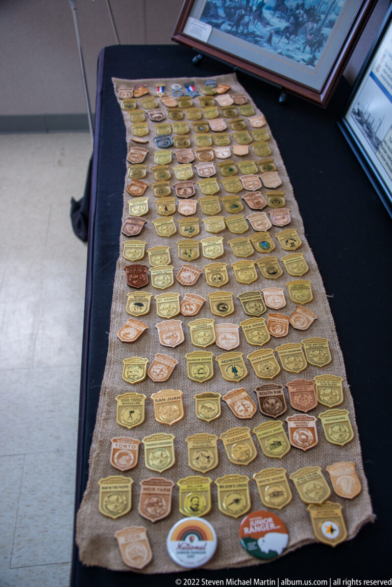 Rows of colorful military-style badges cover a cloth display table inside a museum.