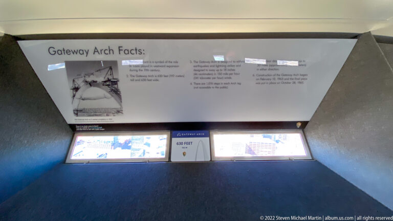 A Gateway Arch facts panel hangs above two illuminated displays in an angled exhibit bay.