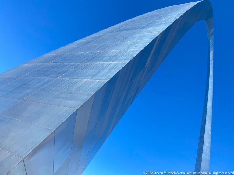 The Gateway Arch’s reflective steel surface curves overhead against a clear blue sky.