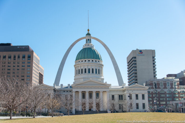 The Old Courthouse stands beneath the Gateway Arch, framed by downtown buildings and lawn.