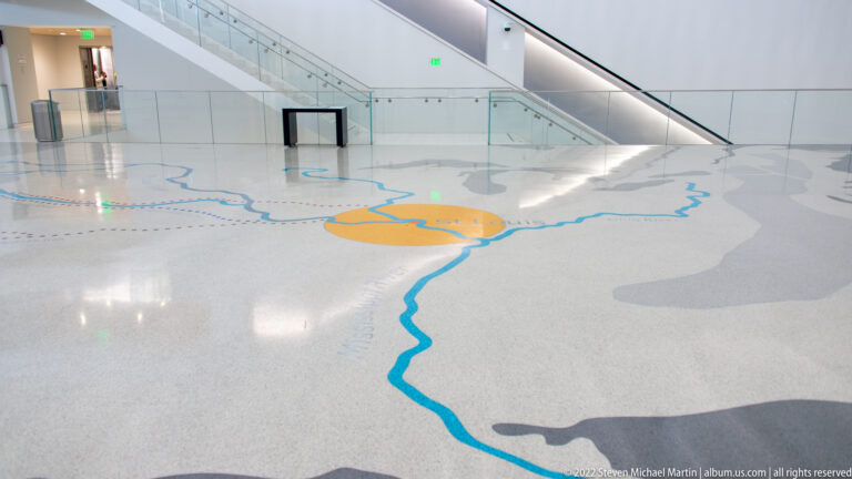 A blue river line crosses a pale floor map toward an orange circular area.