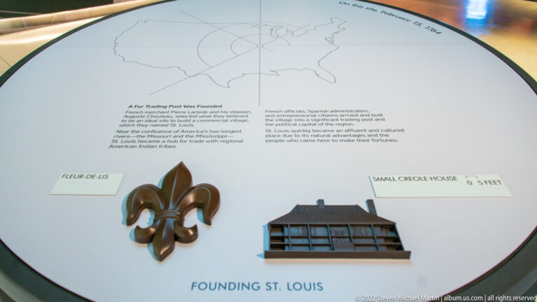 A fleur-de-lis and a small timber-house model sit on a Founding St. Louis exhibit panel.