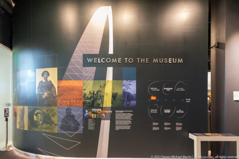 A museum welcome wall combines an arch graphic, historic photographs, and exhibit text.