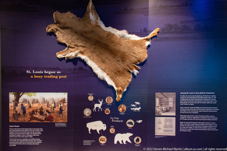 A large animal hide hangs above illustrations and text about fur-trade products.