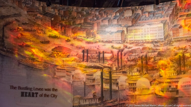 A mural detail shows waterfront buildings, docks, and boats above the caption about the bustling levee.