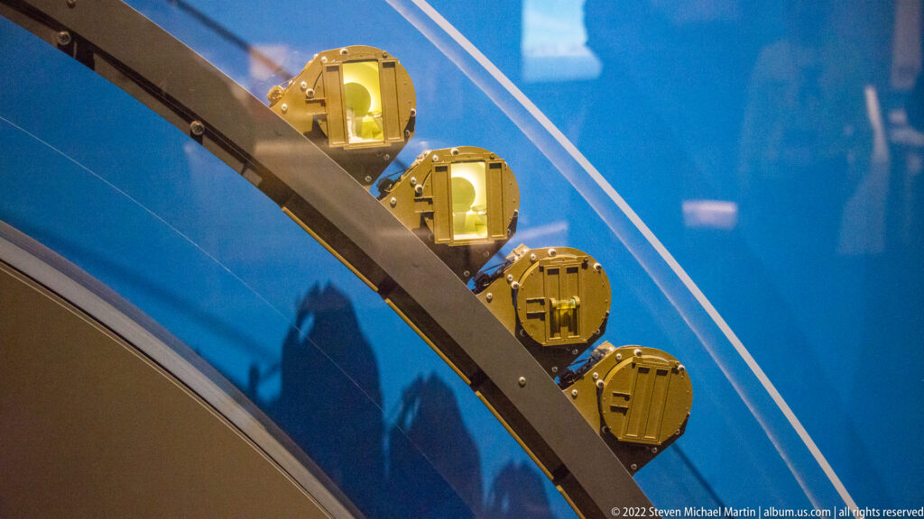 Gold-colored box-like components are mounted in a row along a curved steel segment in a blue display.