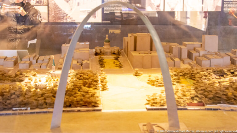 A miniature city model with a central civic building sits beneath a curved Arch-shaped frame.