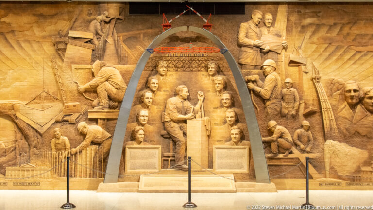 A sculptural relief shows workers and tools around a central group framed by the curve of the Gateway Arch.