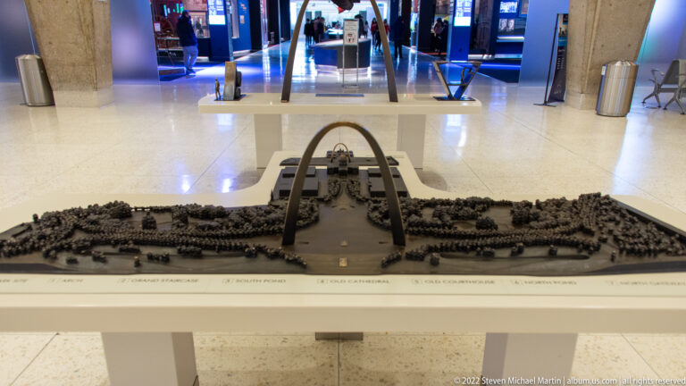 A low model shows the Gateway Arch above a central plaza, surrounded by trees, paths, and city blocks.