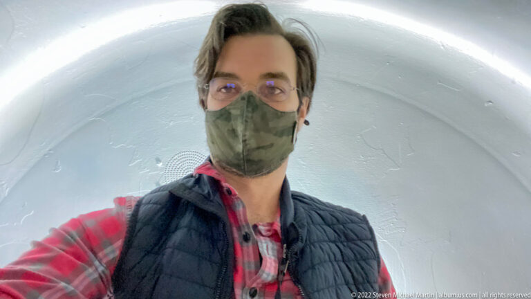 A masked visitor takes a close selfie inside a small white curved compartment.