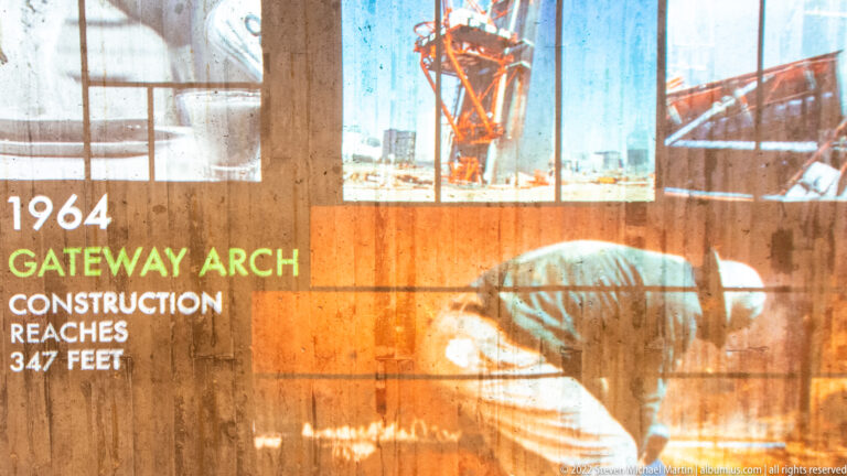 An exhibit image shows a worker and steel framework beneath text stating the Arch reached 347 feet in 1964.