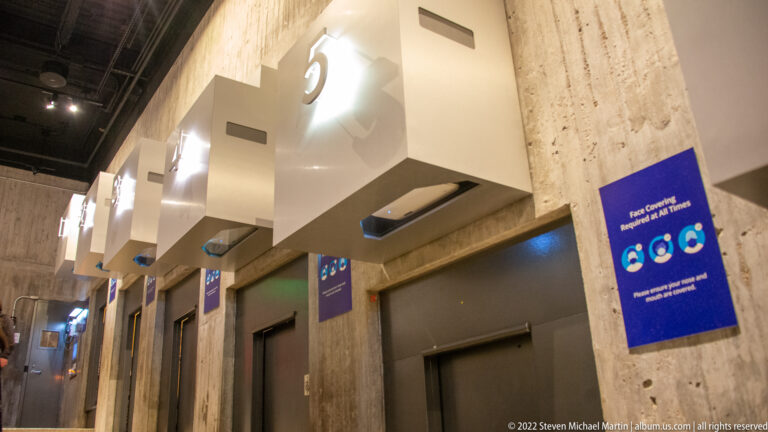 Restroom doors with large numbered signs line a concrete corridor, with face-covering notices between the entrances.