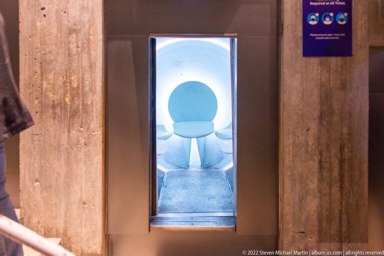 A white urinal is visible through a narrow opening between concrete restroom partitions.