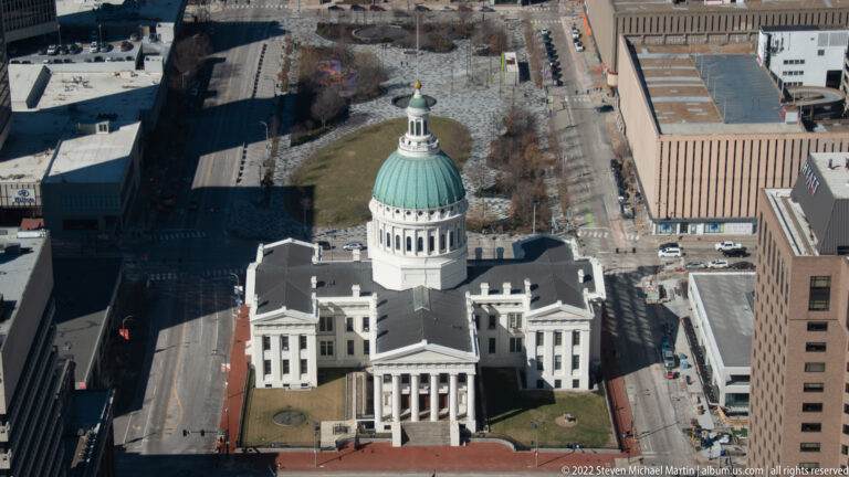 An aerial view centers the Old Courthouse’s green dome and white rotunda among downtown St. Louis buildings.