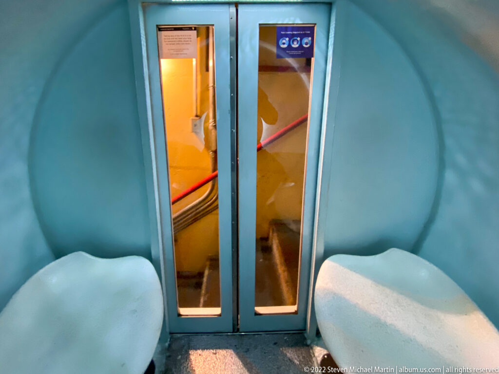 Two narrow doors divide a blue tram cabin with pale molded seats on either side.