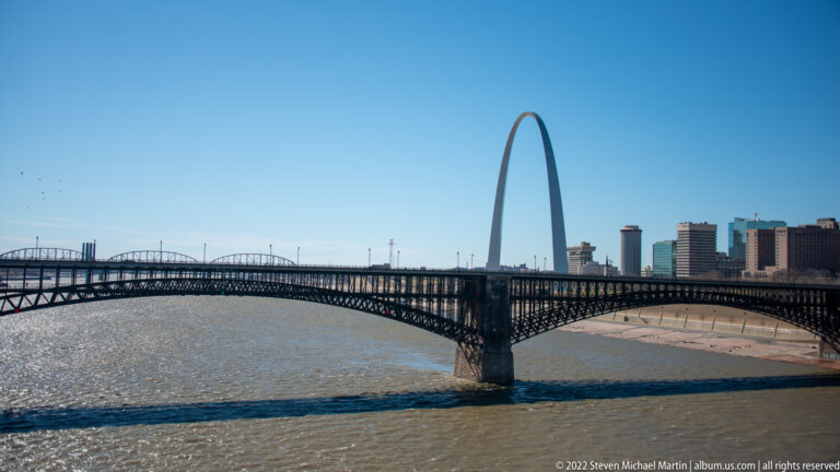 The Gateway Arch stands beyond the Mississippi River and Eads Bridge, with downtown St. Louis along the waterfront.