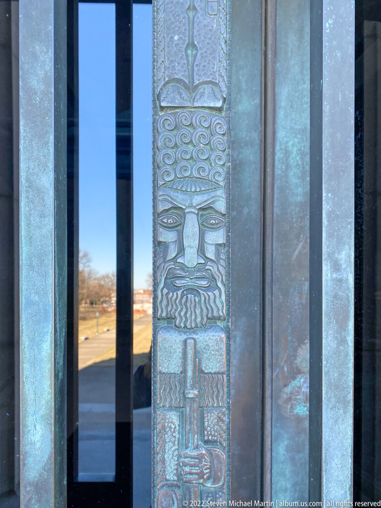 A stylized face and geometric patterns run down a narrow metal panel beside glass.