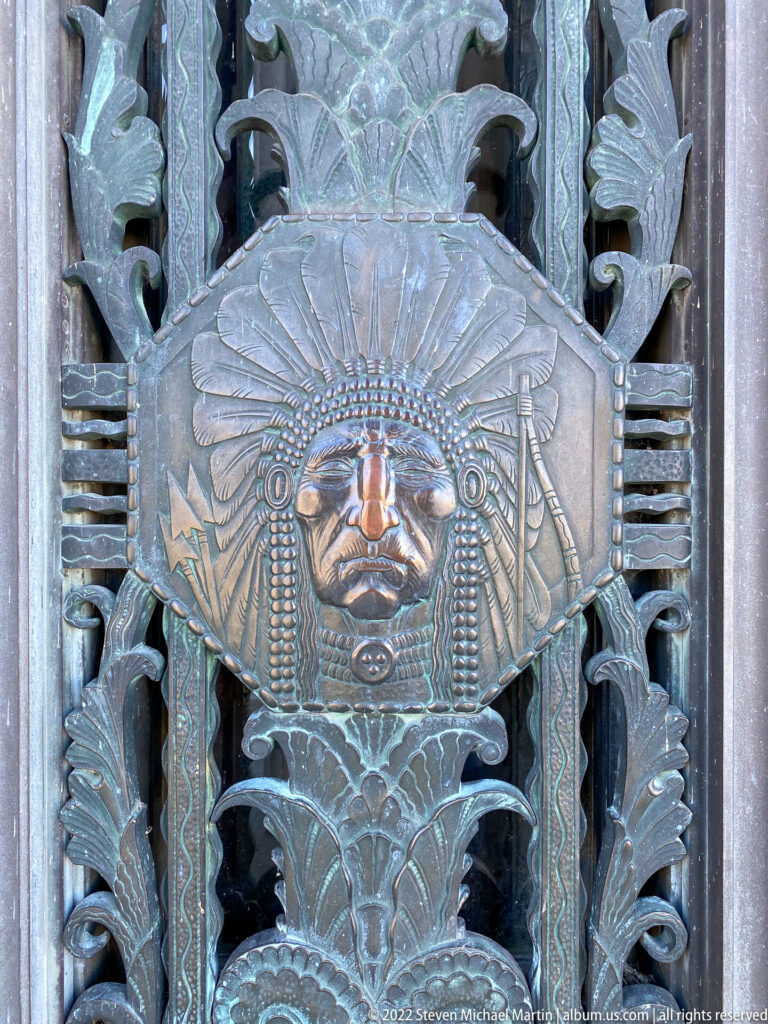 A raised face with a radiating headdress appears within ornate metal foliage.