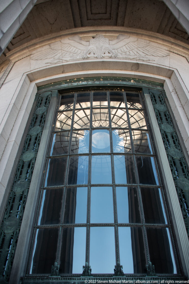A tall gridded window reflects the dome within a carved stone entrance surround.