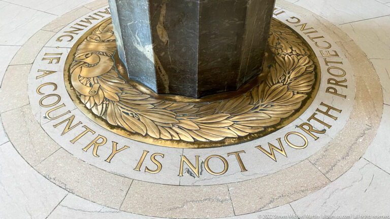 A bronze wreath and partial inscription encircle a dark pedestal on the memorial floor.