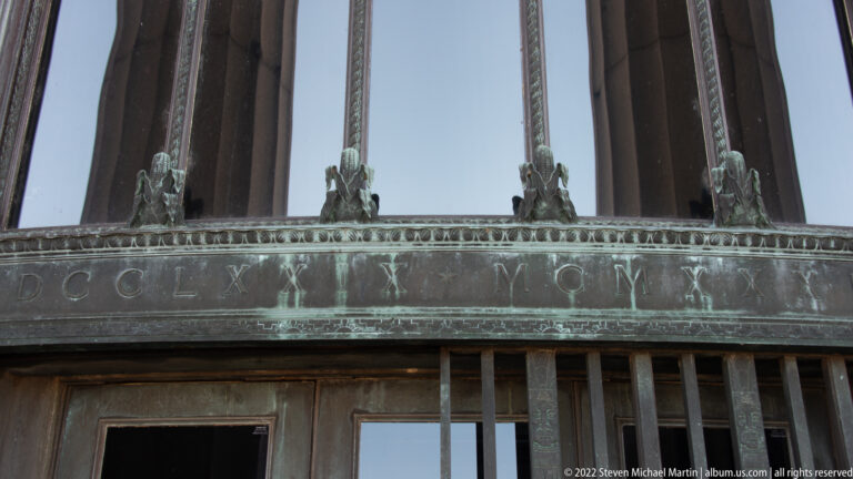 Low-angle view of bronze lettering and small figures above the memorial’s glass entrance doors.