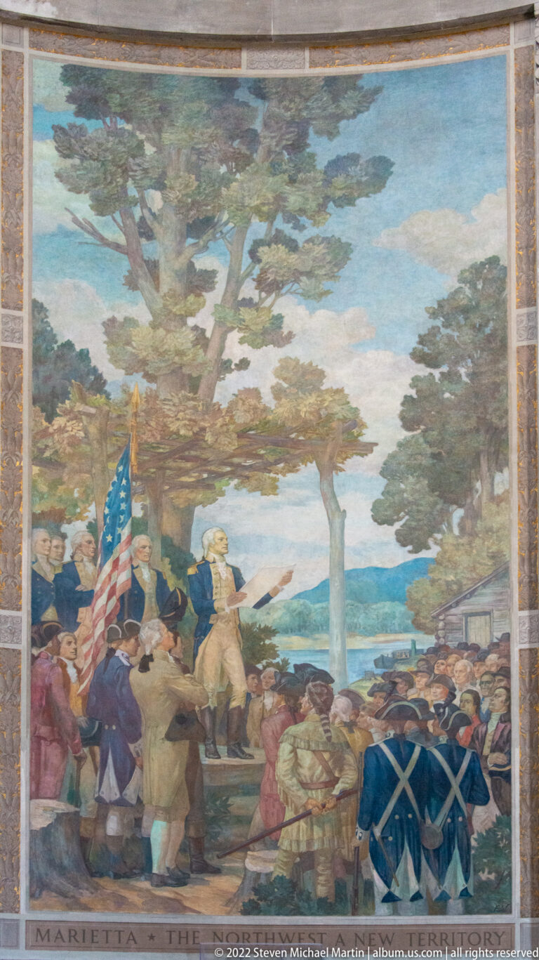 Mural labeled “Marietta” shows a crowd beneath trees, with an American flag and uniformed figures.