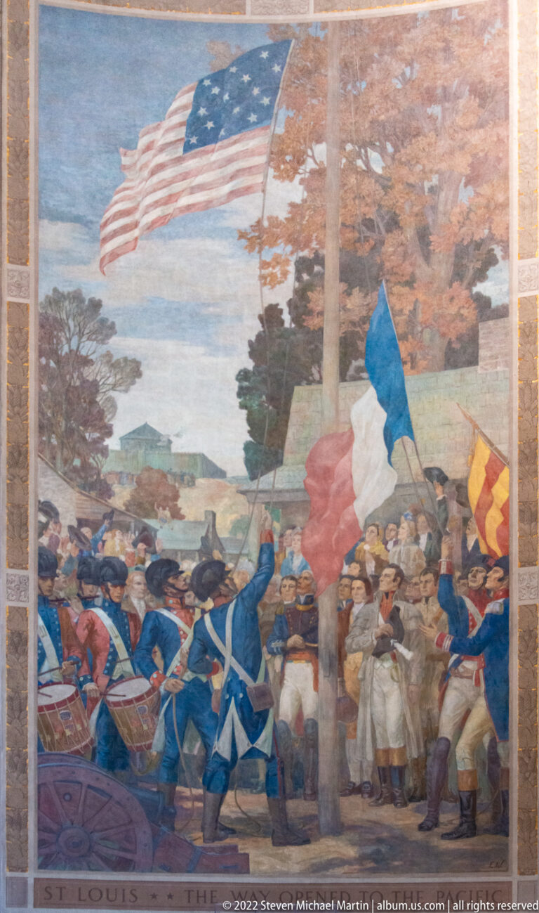 Mural labeled “St. Louis” shows a crowd raising American and other flags beneath trees.