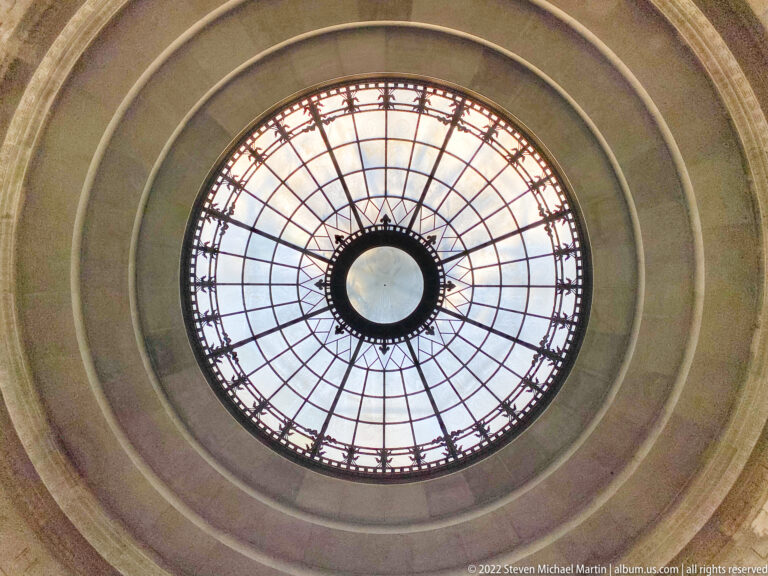 A circular glass oculus with radial metal framing sits within concentric stone rings.
