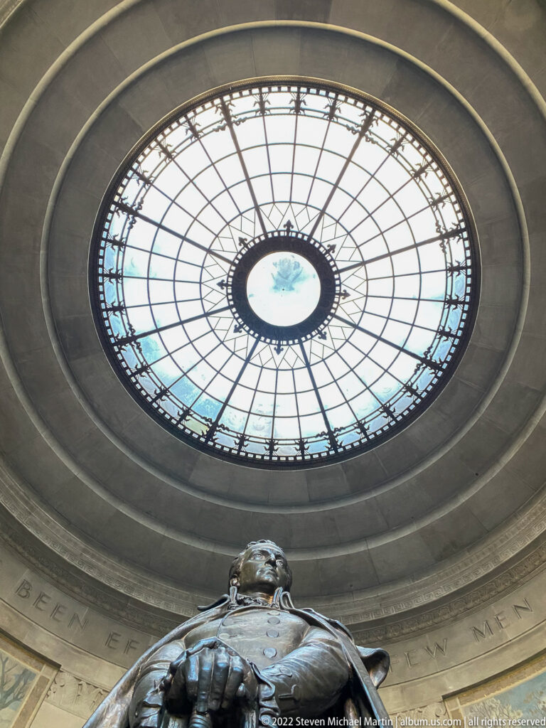 A bronze statue rises beneath the large circular oculus and curved interior inscription.