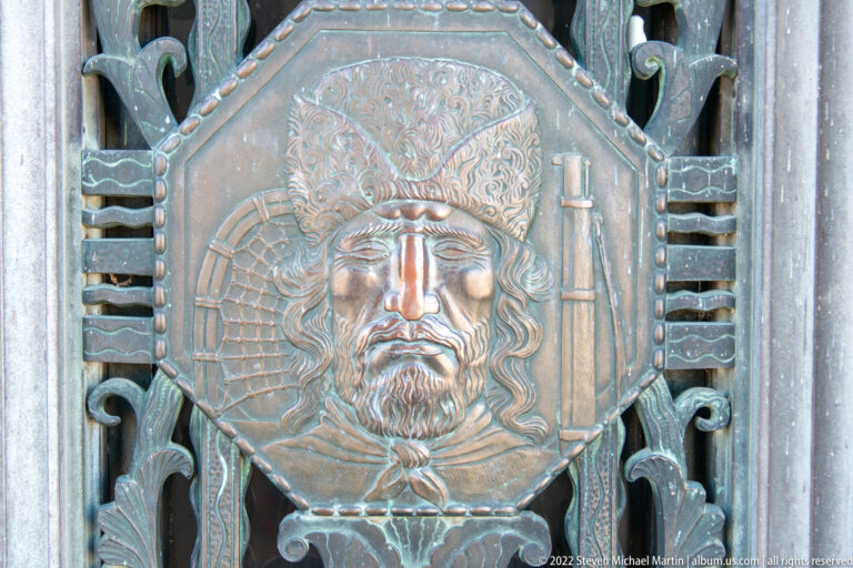 A circular bronze relief shows a bearded face beneath an ornate headdress, surrounded by patterned metalwork.
