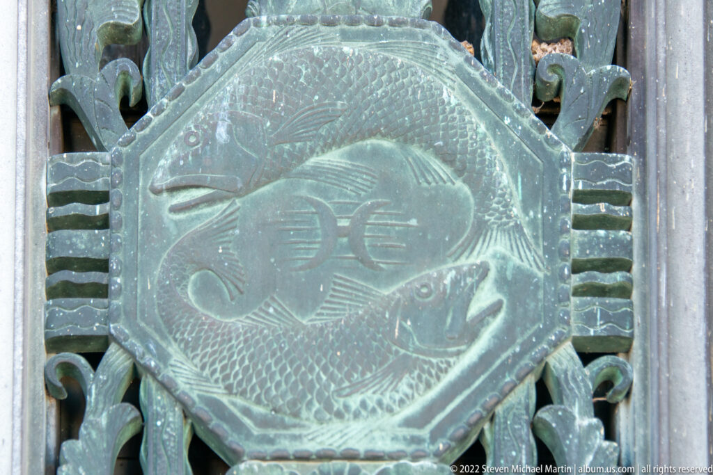 A bronze relief of a large fish fills a circular panel bordered by ornamental metalwork.