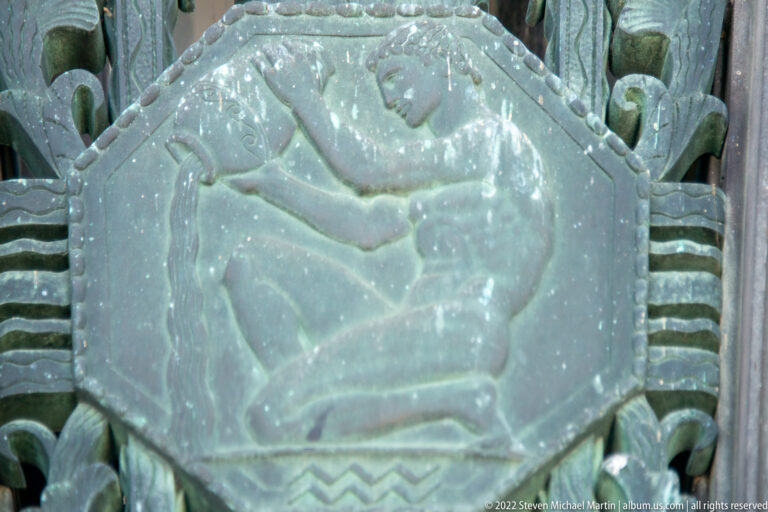 A spread-winged bird appears in a circular bronze relief surrounded by patterned metalwork.