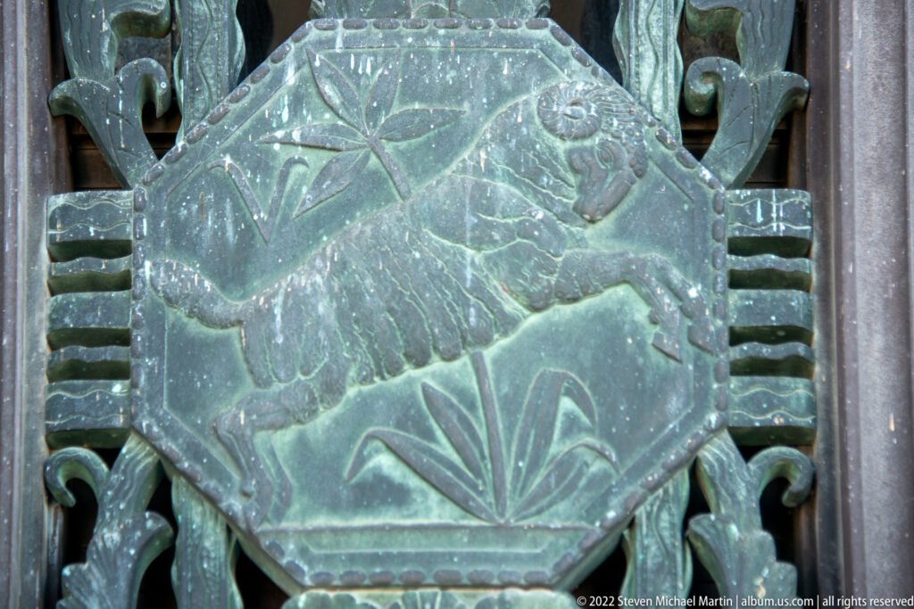 A four-legged animal appears in profile on a weathered bronze panel with foliage-like details.