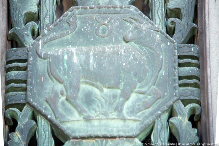 A broad-bodied animal with a lowered head is carved in relief on a patinated bronze panel.