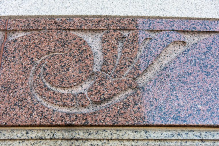 A small carved motif appears in a rectangular inset within a speckled pink-and-gray stone band.