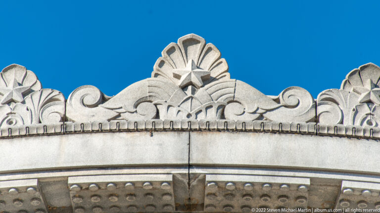 A carved stone crest with a central starburst and scrolls crowns a façade above a projecting cornice.